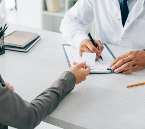 Revenue Cycle Solutions - Patient giving doctor piece of paper while doctor writes down on his clipboard